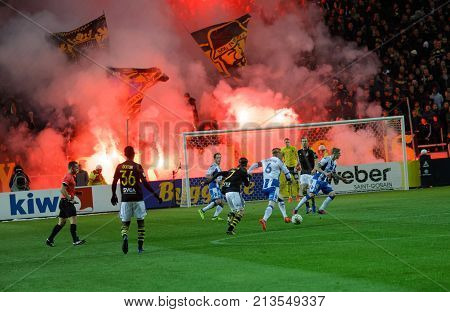SOLNA SWEDEN - OCT 30 2017: The supporters to the soccer team AIK waving flags starting red fire giving lots of smoke. October 30 2017SolnaSweden