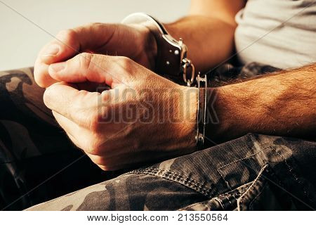Handcuffed soldier in military army clothes. Prisoner of war or arrested terrorist close up of hands in handcuffs selective focus.