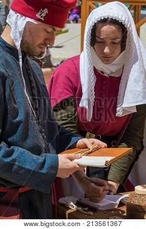 Medieval reenactors in scribe costumes practicing traditional illumination writing calligraphy with feather quill and ink, Mdina, Malta, April 2017