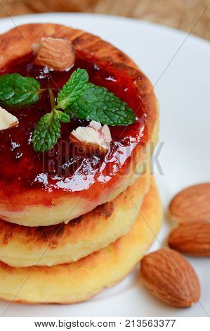 Curd cakes. Fried curd cakes with jam and almonds on a white plate. Traditional ukrainian dessert syrniki recipe. Vertical photo. Closeup