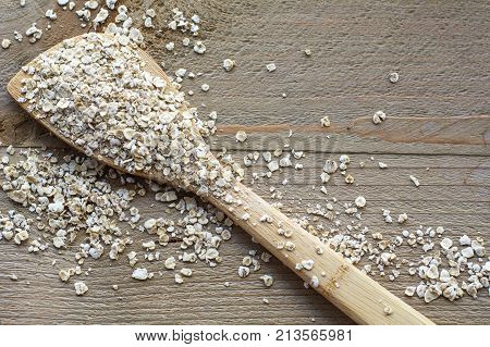 One wooden spoon with many raw cereals is on the brown wooden background
