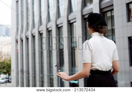 Stylish young female office worker in classic outfit in the city center wearing white turtle neck black beret and cardigan. Business city coffee break.