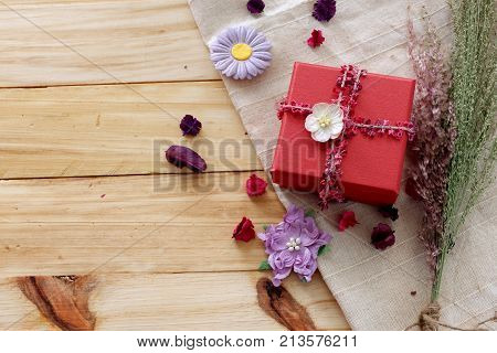 Red gift box with beautiful bow ,grass flower on white fabric on wood board background,top view for copy space