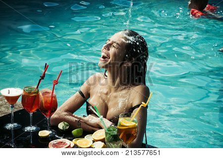 Cocktail and sexy girl in pool. Summer vacation and party. Woman with alcoholic beverage and fruit. Swimming and relax in water pool. Drink food and happiness.