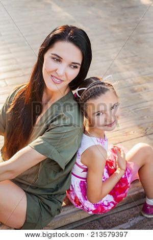 Beautiful mother and daughter sitting outdoors on steps, laughting and having fun. Concept of happy family