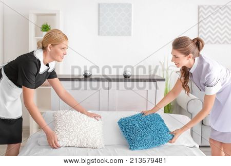 Chambermaid teaching trainee to make bed in room