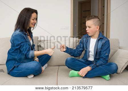 Happy mother and son sitting on sofa and playing rock paper scissors at home