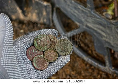 Old coins on the hand in the glove above the metal detector coil