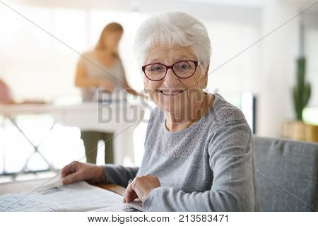Portrait of old woman reading newspaper while homehelp irons