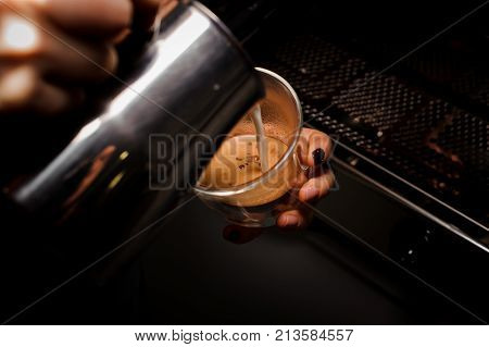 Female hands pouring milk from pitcher into the coffee cup against the coffee machine. Coffee concept