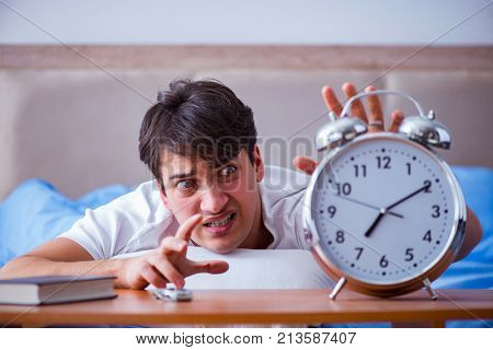 Man in bed frustrated suffering from insomnia with an alarm cloc