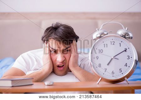 Man in bed frustrated suffering from insomnia with an alarm cloc