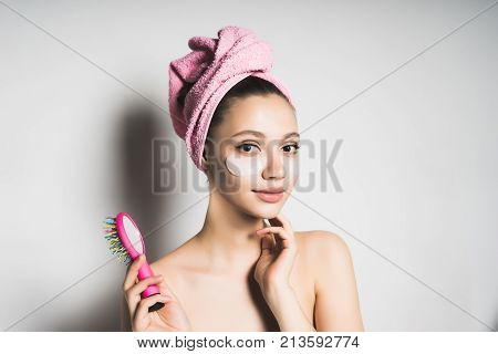 attractive young girl looks after the skin on her face, on her head a pink towel looks to the camera