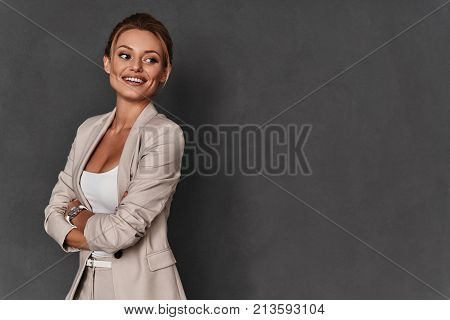 Always confident. Attractive young woman in smart casual wear keeping arms crossed and smiling while standing against grey background