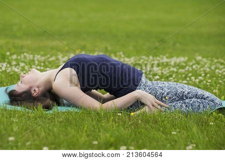 Thin girl doing yoga outside at summer on green grass. Fish pose matyasana