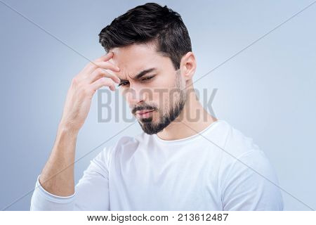 Thoughtful person. Calm serious young man looking concentrated while touching his head and trying to remember the phone number of his close friend