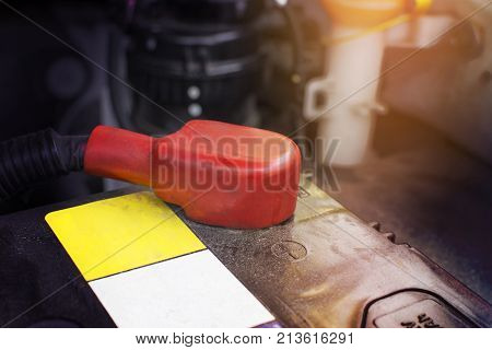 Battery anode terminal with red rubber cover is installed on a black battery in a electric system of car engine. Automotive parts concept.