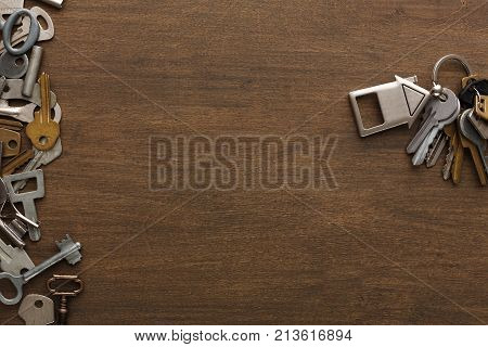 Bunch of keys with house shaped trinklet against wooden background and collection of different keys. Safety, security and real estate concept, top view, copy space