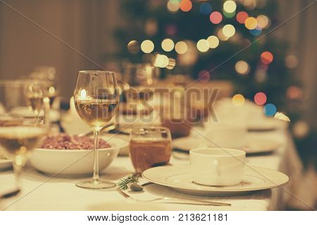 Dining table full of a variety of delicious festive food and wine with a Christmas tree in the background in home with vintage mood