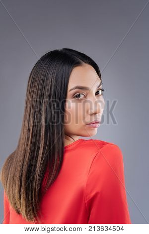 Kind glance. Adorable young woman looking great in her gorgeous red dress while going for a walk and turning her head to see the people behind her back