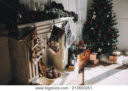A beautiful and nice picture of a festive decoreted fireplace covered with socks for gifts, candles, bemps, glitter and another small things that makes this place be so comfortable and cozy. Also there is a Christmas tree in one of the room's corner.