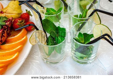 Fresh fruits and berries of different bright colors cut in small pieces are served on a table with mohito cocktail