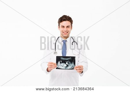Portrait of a cheerful young male doctor with stethoscope dressed in uniform holding x-ray photograph and looking at camera isolated over white background