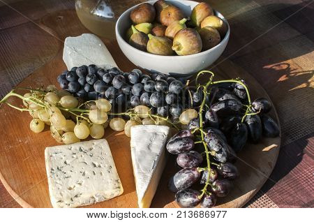 Wooden plateau with fresh grapes figs and types of cheese closeup as homefood background