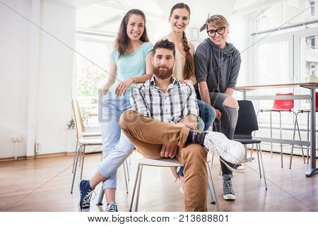 Portrait of four co-workers smiling and looking at camera while wearing cool casual clothes during work, in the shared office space of a modern hub for freelancers and young entrepreneurs
