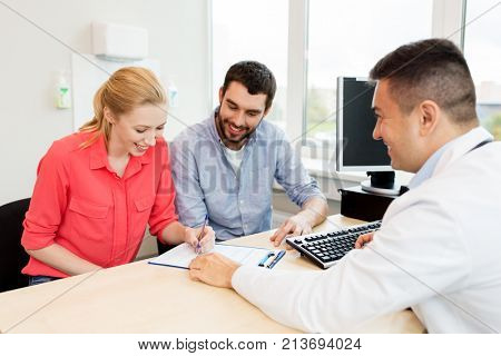 family planning, medicine, fertility and healthcare concept - happy couple visiting doctor and filling form at clinic