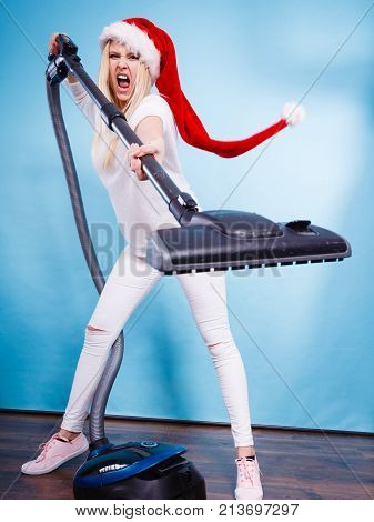 Woman vacuuming the house last minute. Teen girl in santa helper hat with vacuum cleaner angry furious face expression. Christmas time and housework concept.