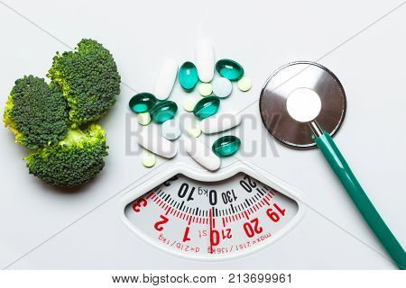 Diet healthy eating weight control and health care concept. Closeup green broccoli stethoscope pills on white scales choice between