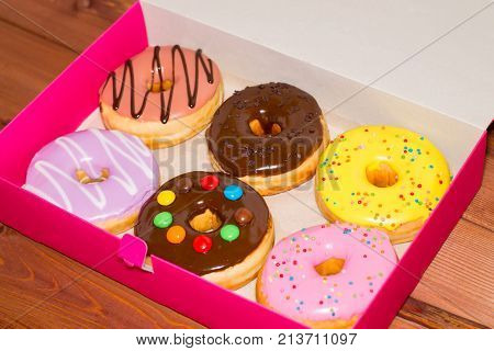 Six colored donuts in a pink box on a wooden background. Sweet donuts with glaze.