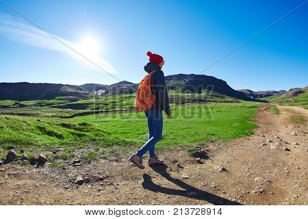 back view of woman traveler with small orange backpack on a walk in the Valley of the river of Hveragerdi Iceland. Hiking Tour of Reykjadalur Hot Springs