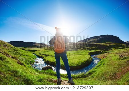 back view of woman traveler with small orange backpack on a walk in the Valley of the river of Hveragerdi Iceland. Hiking Tour of Reykjadalur Hot Springs