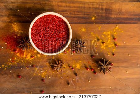 Close up white wooden bowl filled with paprika powder on dark wooden surface covered with anise and turmeric