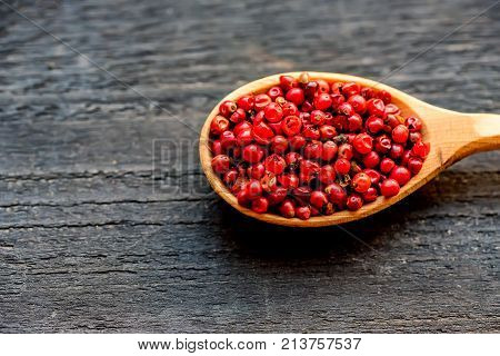 Close up wooden spoon with pink peppercorn on dark background