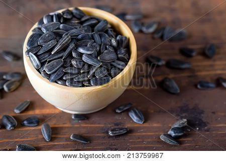 Close up unpeeled sunflower seeds in wooden bowl on dark wooden table
