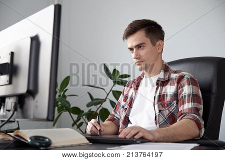 portrait of a young designer freelancer student engaged in creative work at your working place holding a stylus and using the tablet.
