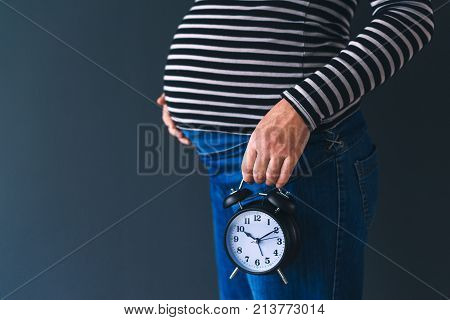 Pregnant female with vintage alarm clock expecting baby in third trimester of pregnancy