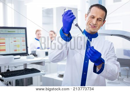 Satisfied with results. Budding cheerful male laboratorian  smiling to himself looking at the vial while holding it