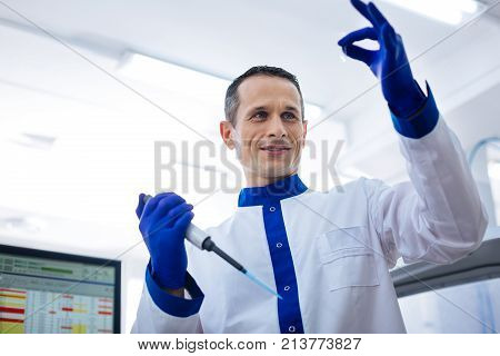 Perfect level. Experienced  appealing medical worker evaluating the level of liquid in the small glassware holding pipette while wearing labcoat