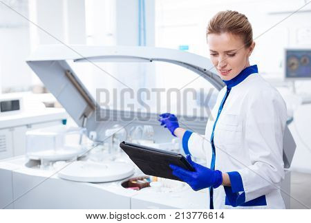 Brave experiment. Promising pleasant female researcher holding with one hand and looking at the tablet and considering about new experiment