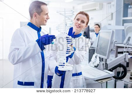 Molecule organization. Happy glad male and female team of scientist examining molecules in DNA and smiling while posing in the lab
