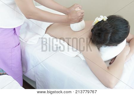 Female therapist using steamed Thai Herbal Compresses to relieve pain and inflammation for young Asian client Thai traditional massage in Spa salon