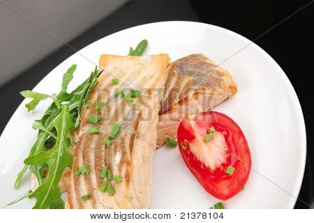 sunde fisk retter: bagt pink laks bøffer garneret med tomater og rocula på hvid parabol er