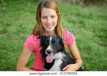 Smiling Happy Girl Wearing Pink Shirt Hugging with Her White and Black Dog in the Park During Sunny Summer Day Outdoors