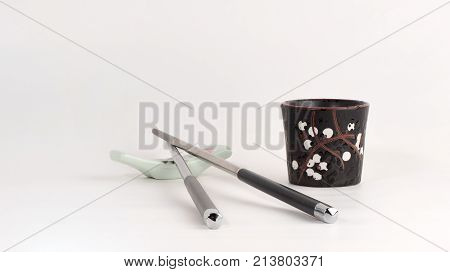 Staсk. Metal chopsticks on porcelan "lion" chopsticks rest and black sake glass. White background. Front view
