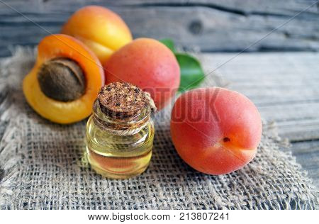 The apricot kernel oi in a glass jar and fresh ripe apricots on old wooden background. Essential apricot oil for spa,beauty treatment, aromatherapy and bodycare.Selective focus.