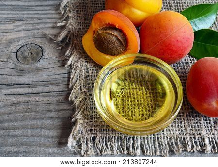 The apricot kernel oi in a glass bowl and fresh ripe apricots on old wooden background. Essential apricot oil for spa,beauty treatment, aromatherapy and bodycare.Selective focus.